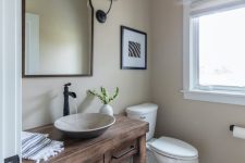 a vintage farmhouse bathroom with greige walls and a light-stained wooden floor, a reclaimed wood vanity, a catchy sink and black fixtures