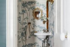 a vintage powder room under the stairs with botanical wallpaper, a mosaic tile floor, a corner wall-mounted sink and gold touches