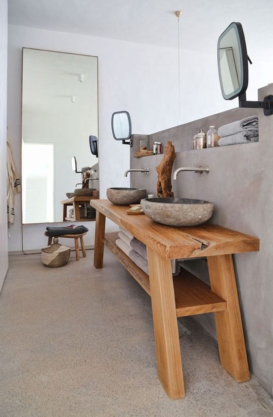 a wabi sabi bathroom with a concrete floor and wall with a built in shelf, a wooden vanity with stone carved sinks and a mirror