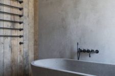 a wabi-sabi bathroom with concrete walls, a floor and an oval tub, a reclaimed wood wall, black fixtures for a more modern feel