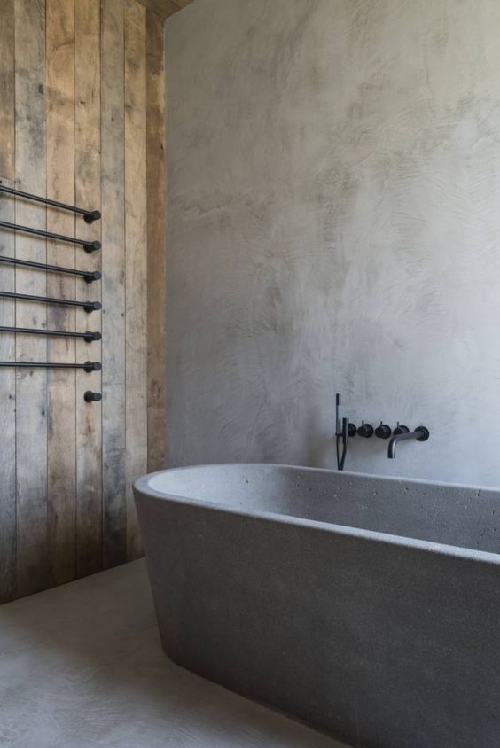 a wabi-sabi bathroom with concrete walls, a floor and an oval tub, a reclaimed wood wall, black fixtures for a more modern feel