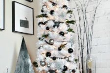 a white Christmas tree decorated with black and silver ornaments, evergreens, snowflakes, a wooden star topper