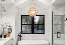 a white modern farmhouse bathroom with skylights, a large vanity, an oval tub, a wood floor and some black touches for drama