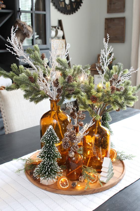 a woodland Christmas centerpiece of evergreens and pinecones in amber bottles, bottlebrush trees and lights