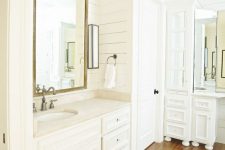 an all-white bathroom with white planked wlals, white furniture and a rich-stained hardwood floor plus vintage fixtures is pure chic