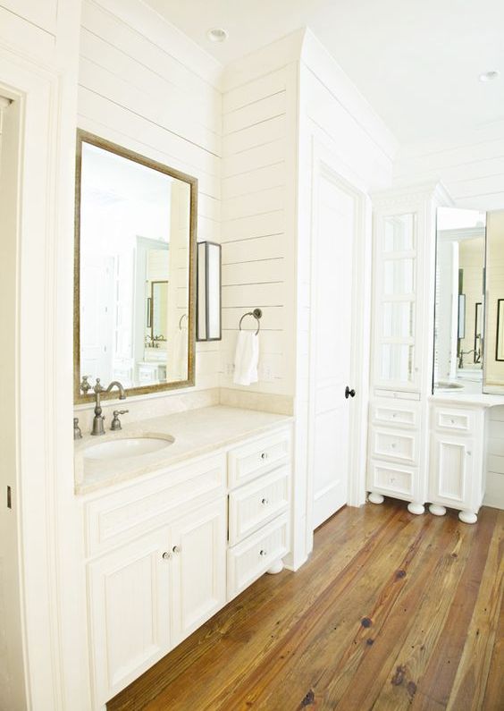 an all-white bathroom with white planked wlals, white furniture and a rich-stained hardwood floor plus vintage fixtures is pure chic
