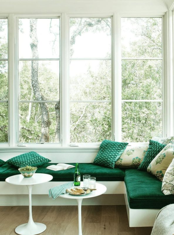 an amazing breakfast nook with a floating banquette with green upholstery, glazed walls, small white tables