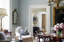 an elegant English country living room with white wainscoting and crown molding, with chic vintage furniture and a brass chandelier
