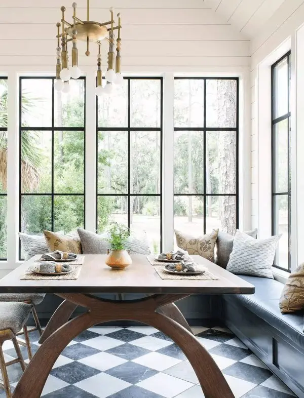 an elegant eating space by a whole gallery of windows, a grey banquette seating, printed pillows, a stained table