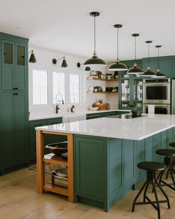 an emerald kitchen with shaker-style cabinets, white stone countertops, black pendant lamps and sconces and black stools