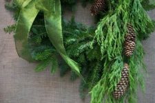 an evergreen wreath with a large green bow and some pinecones is a pretty decoration for Christmas