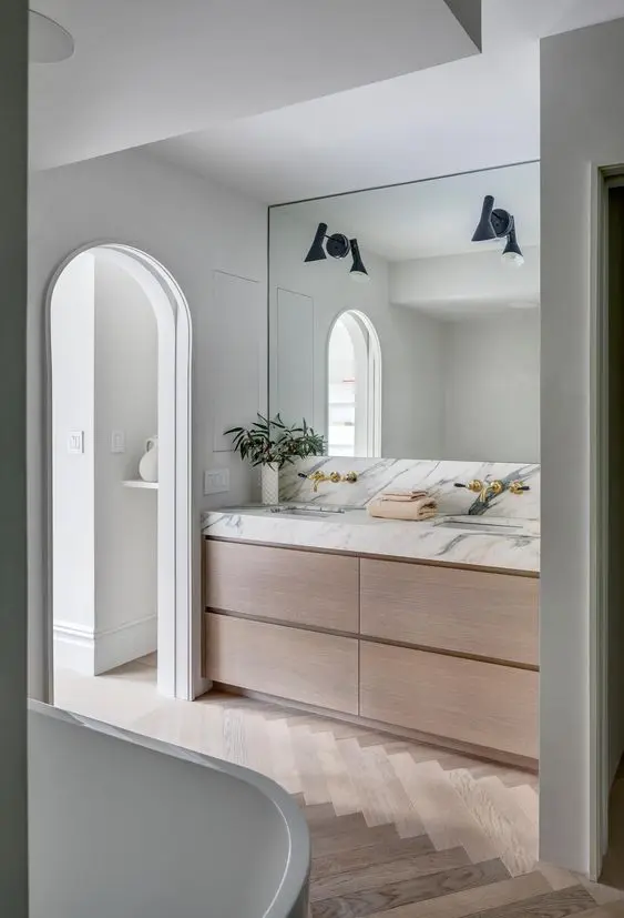 an exquisite contemporary bathroom with a light-stained parquet floor, a light-stained sleek vanity with a white marble countertop and black sconces