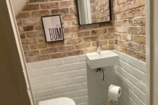 an industrial under the stairs powder room with brick walls and white subway tiles, a printed tile floor and a wall-mounted sink