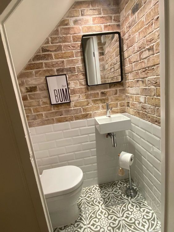 an industrial under the stairs powder room with brick walls and white subway tiles, a printed tile floor and a wall-mounted sink