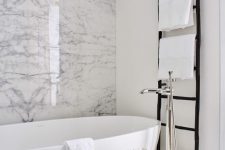 monochromatic chic with a white marble wall, an oval tub, a black ladder and a printed side table