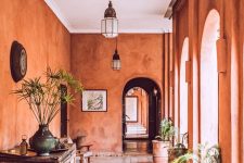 02 a fabulous Moroccan space with rust-colored plaster walls, a vintage wooden console table, potted plants and cool pendant lamps