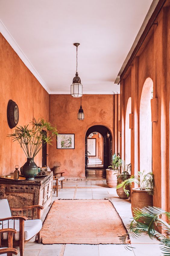 a fabulous Moroccan space with rust colored plaster walls, a vintage wooden console table, potted plants and cool pendant lamps