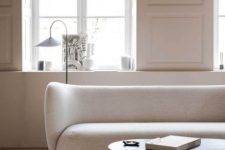 07 a refined and chic space with paneled walls, a delicate curved creamy sofa, a curved coffee table, a catchy floor lamp and a pendant bulb