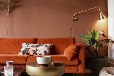 08 a beautiful earthy tone living room with brown walls, a rust-colored sofa, a gold side table and a gold sconce and potted greenery