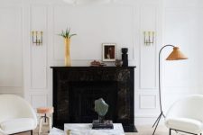 08 a sophisticated living room with white paneled walls, a black marble fireplace, a duo of geometric white marble tables and chairs with rounded backs