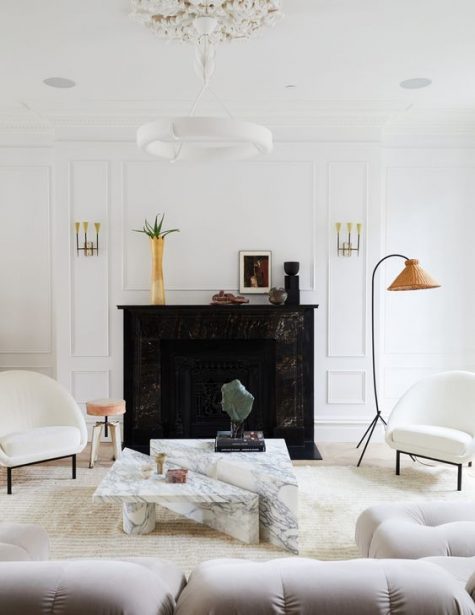 a sophisticated living room with white paneled walls, a black marble fireplace, a duo of geometric white marble tables and chairs with rounded backs