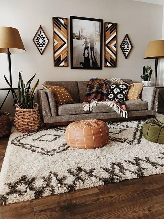 a bold African inspired interior with a grey sofa and earthy pillows and blankets, poufs, tan floor lamps and potted plants