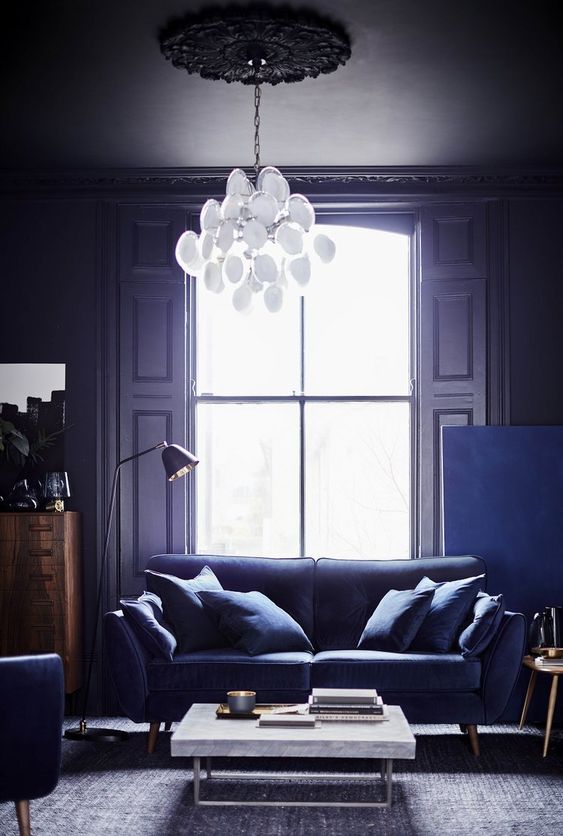 a fantastic very peri living room with a purple sofa and chairs, a stone coffee table and a catchy chandelier
