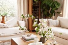 19 a warm neutral living room done in soft creamy shades, with light-stained furniture, potted plants and blooms and a printed rug