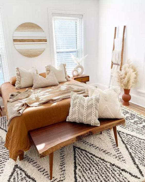 a cool warm neutral boho bedroom with a rich-stained bench and nightstands, a bed with neutral and rust bedding, pampas grass