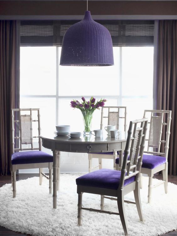 a chic dining space with a round grey table, grey and very peri chairs, a very peri woven pendant lamp and much light