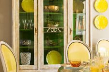 23 a vintage dining room with a beautiful buffet, a vintage table with a glass tabletop, sunny yellow chairs and plates