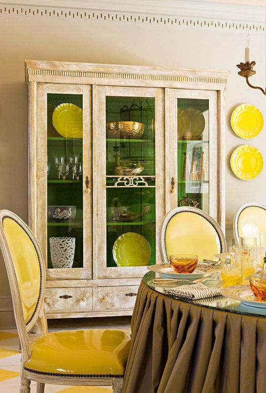 a vintage dining room with a beautiful buffet, a vintage table with a glass tabletop, sunny yellow chairs and plates