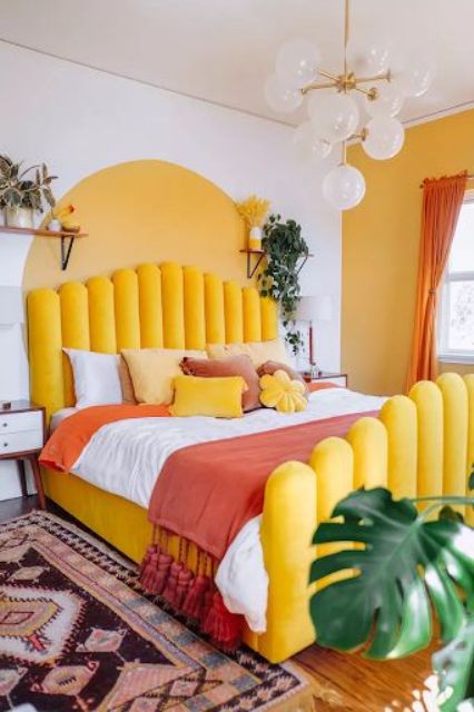 a bright bedroom with a sunny yellow wall and an accent, a yellow upholstered bed, red touches and potted greenery