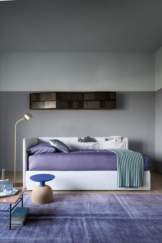 a contemporary space with grey walls, a minimalist daybed with very peri bedding and a matching rug, several coffee tables