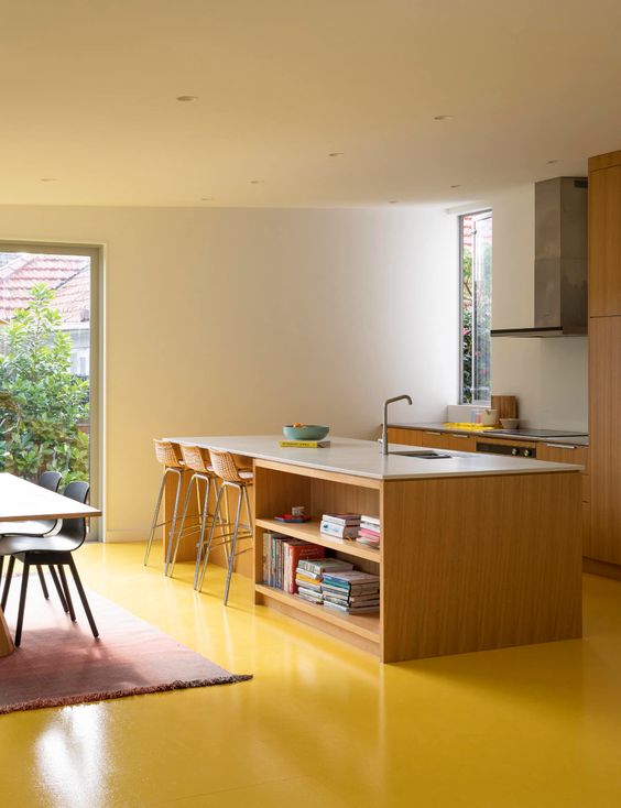 a contemporary kitchen with plain light stained cabinets and a kitchen island, a sunny yellow floor that makes a statement