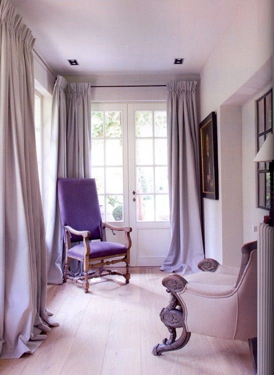 a delicate blush space with lavender curtains, a blush chair and a purple one, some art and lots of light