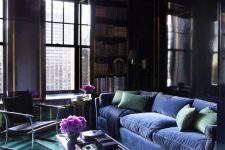 26 a moody living room with deep purple walls, touches of gold, built-in bookcases, a very peri velvet sofa and a green and very peri geo rug
