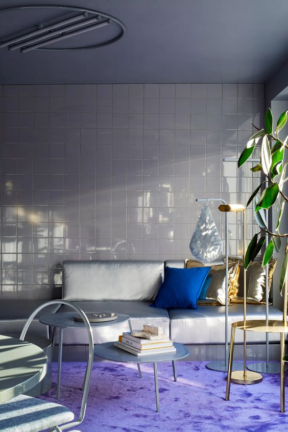a neutral space with a tiled wall, a grey sofa, a very peri rug for a super bold accent, gold pillows and a bold blue one