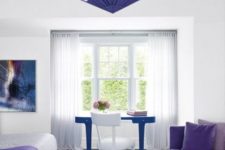 29 a neutral space with a white bed with a very peri blanket, a very peri daybed, a bold violet chandelier and a blue desk