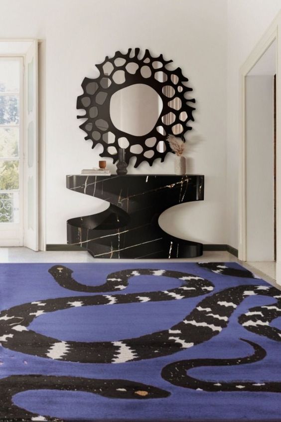 a refined entryway with a very peri snake print rug, a black marble console table and a mirror in an ornated frame