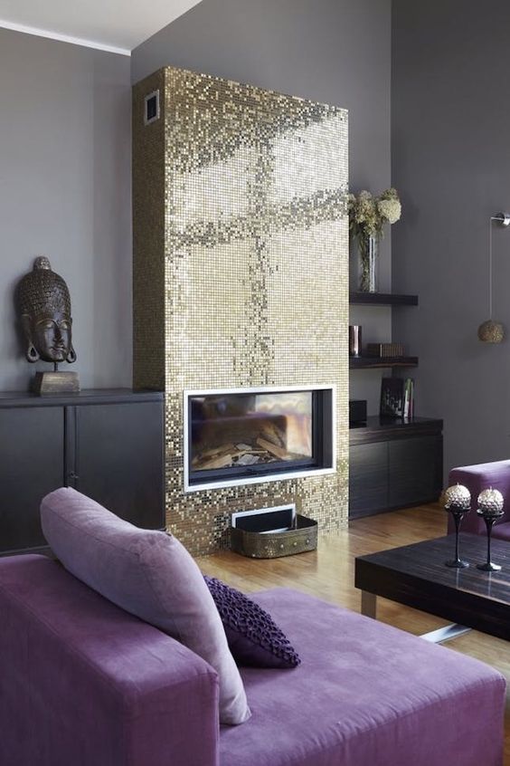 an eclectic living room with grey walls, very peri chairs, a black table, a shiny gold tile fireplace and Asian art