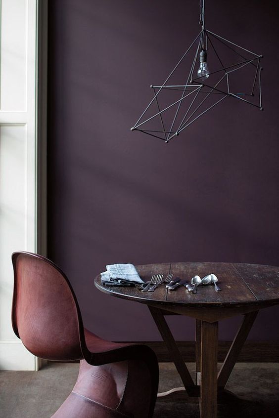 a refined nook with a deep purple accent wall, a stained round table, a brown leather chair and a geometric pendant lamp