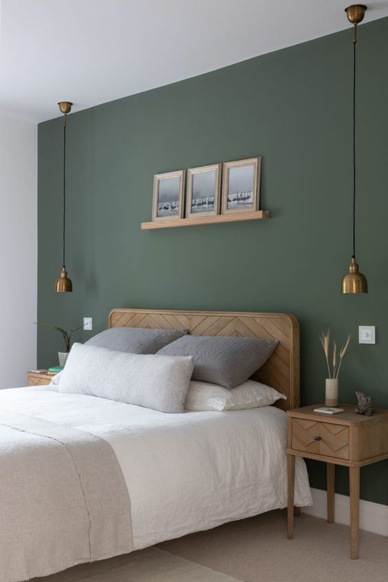 a delicate bedroom with a sage green accent wall, a wooden bed and nightstands, brass pendant lamps and artwork