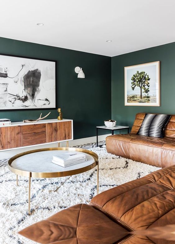 a dark green living room with brown leather sofas, a chic credenza, artwork and brass touches for more elegance