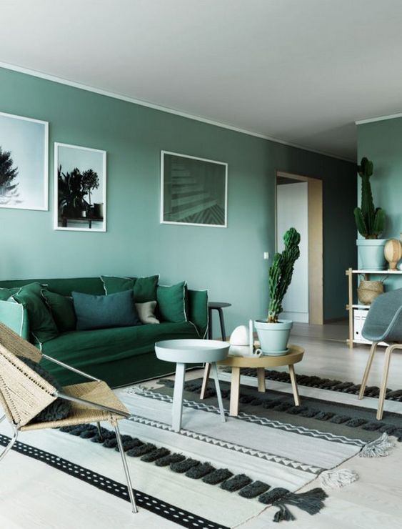 a cool light green living room with an emerald sofa and pillows, a Moroccan rug, simple chairs and side tables