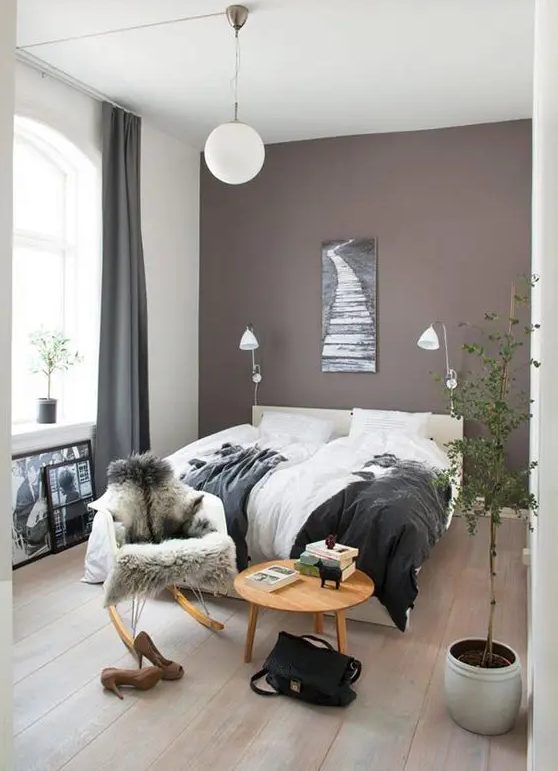 a beautiful boho bedroom with a taupe accent wall, a creamy upholstered bed and lovely bedding, a round table and a chair, a potted plant