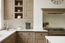 a beautiful intage taupe kitchen with shaker cabinets, white countertops and a backsplash, a cooker with a hood, a catchy clock and vintage knobs