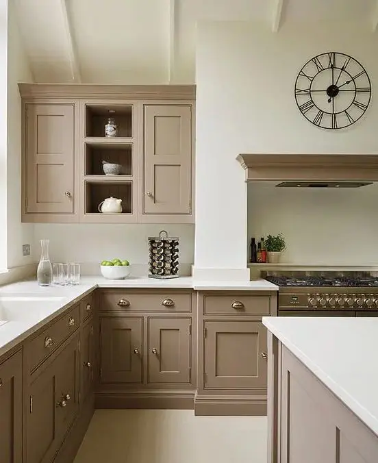 a beautiful intage taupe kitchen with shaker cabinets, white countertops and a backsplash, a cooker with a hood, a catchy clock and vintage knobs