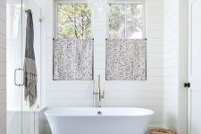a beautiful master bathroom with shiplap walls, ample natural light, and a free-standing soaking tub
