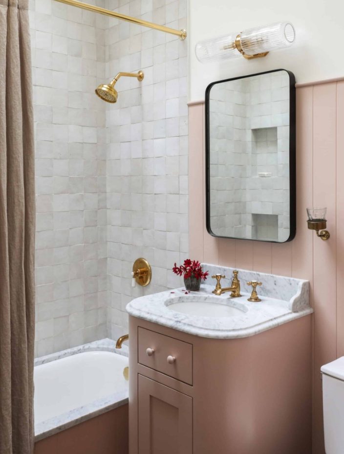 a beautiful modern bathroom with a dusty pink vanity, wall and curtain, white Zellige tiles and gold fixtures
